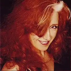 color headshot photo of Bonnie Raitt smiling with hair over one eye