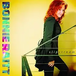 photo of Bonnie Raitt in green bustle back jacket climbing stairs with bright yellow background