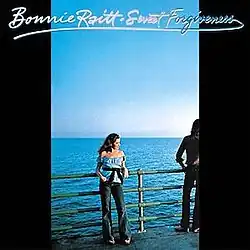 photo of Bonnie Raitt in blue top leaning on railing next to expanse of water near man half off camera