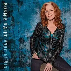 photo of Bonnie Raitt in blue shirt with black jacket against blue-black dapple background