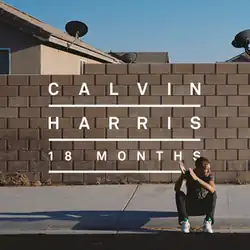 Harris sits on the sidewalk behind a brick fence with a house in the background.