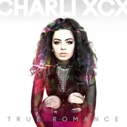 Charli xcx looks at the camera in front of a white background. She is wearing a sheer black shirt and ripped black jeans. Colourful glitch effects are superimposed on the image. White and grey text reads: "Charli XCX – True Romance".