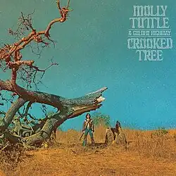 long-distance photo of Molly Tuttle with guitar standing next to fallen crooked tree
