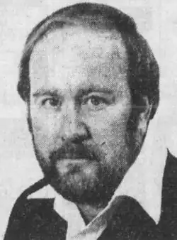 Black and white photo of a middle-aged man with a beard, wearing a white dress shirt and dark jacket