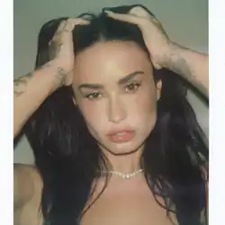 Close-up of Lovato holding their long black hair upwards with both hands.