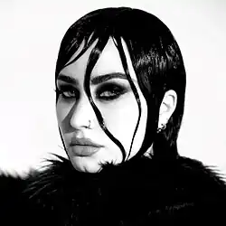 A black and white picture of Lovato looking into the camera with gelled strands of hair around her eye