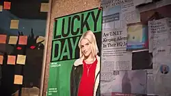 On a bulletin board, a poster advertising a podcast with a photo of Ruby and reading "Lucky Day with Conrad Clark" is featured along with several news headlines.