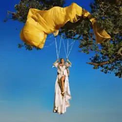 A woman dangling in the air, suspended by a yellow parachute caught in the branches of a tree.