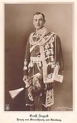 Black-and-white portrait of Ernest Augustus, Duke of Brunswick and Lüneburg, wearing an ornate military uniform with decorations and holding a plumed hat, photographed during his reign between 1913 and 1918.