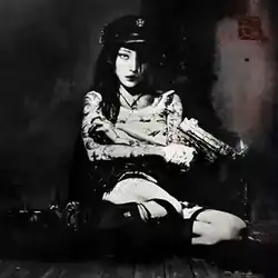 A person sitting with their legs sideways in the middle of the frame. A gun is in their hand, with a small flame coming out of it. The image is composed of black and white stuffs.