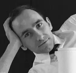 Part of a black and white publicity shot of a half-smiling man in shirtsleeves, looking directly at camera. He holds a mildly eccentric or faux-glamour pose, lying on his side with his head supported on his hand, and one knee akimbo (in the original picture, where he was posing with his crockery design). He has short, dark, receding hair, and dark, expressive eyes.