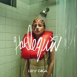 Lady Gaga standing in a shower with orange hair, wearing a white dress and a flotation device around her neck
