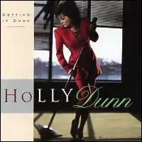 photo of Holly Dunn in red standing leaning microphone on stage in front of windows, looking aside