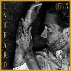 A photo of Hozier covered in dirt and lying in the ground, surrounded by yellow borders. The word "Hozier" is placed in the top-right corner, while the word "Unheard" appears on the left side of the image.