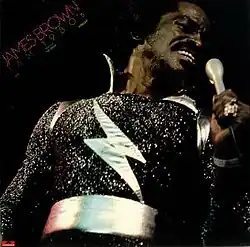 James Brown holding a microphone in a sparkly black sparkly outfit with a white lightning strike on his chest. In the top left "James Brown Jam 1980's" in pink and green text made out of small dots.