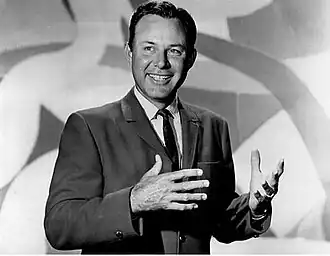 A dark-haired man wearing a jacket and tie, smiling broadly