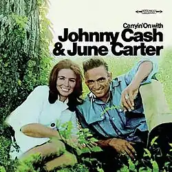 photo of June Carter and Johnny Cash smiling seated at base of tree in woods