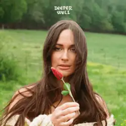 A woman with very long brunet hair holds up a flower against a bucolic green backdrop