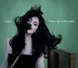 Shot of Lena wearing a black dress and a white necklace. Information on the song is placed on her left and right.