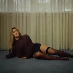 Hilary Duff staring up in brown knitwear, black pants and stockings while lying on the floor