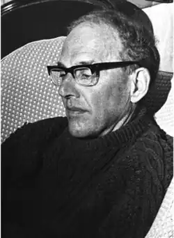 Image of Robertson in middle age, wearing a thick-knitted jumper, and black spectacles. He is slightly balding and sitting down, with a pensive expression.