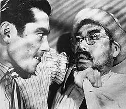 A violent Matsunaga pins Sanada to the wall with his elbow.