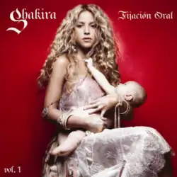 Shakira in a sleeveless white dress that extends past her legs, holding an unclothed infant in her arms, who is reaching at the necklace she is wearing.