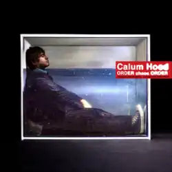 Calum sits in a box wearing a suit with his eyes closed. He is submerged in water up to his neck.