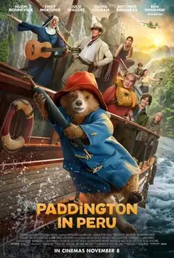 A bear wearing a red hat and a blue coat is hanging off the side of a boat holding on using an umbrella