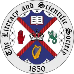 The seal of The Literary and Scientific Society, established 1850. A central shield is quartered and displays four symbols: an open book, a green dragon, a golden harp, and the Red Hand of Ulster, with a crown in the middle. =