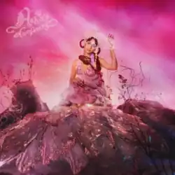 Raveena wearing a pink gown and a golden headdress, sitting on a rock-like formation in a pink-hued landscape with one hand raised. The title, "Asha's Awakening," is written in the top-left corner.