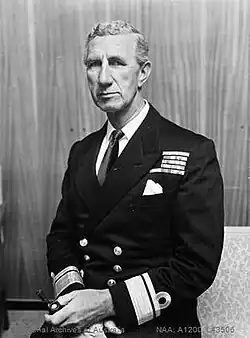 Portrait of a man in naval uniform. Visible from the waist up, he appears to be sitting and wears a dark, formal naval jacket that sports the rank of rear admiral. There are medal ribbons on his left breast, and he is holding a smoking pipe in his left hand.