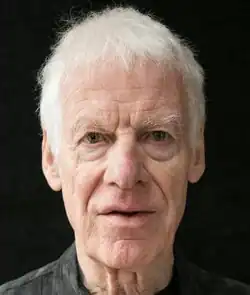 Colour Press headshot of a clean-shaven, elderly man with short white hair. His mouth is open, he is apparently speaking.