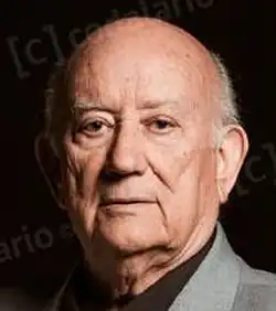 Colour publicity shot of an unsmiling, balding old man