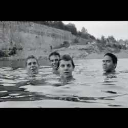 A black-and-white photograph of four men swimming in a quarry lake