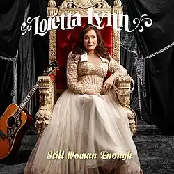 photo of Loretta Lynn in beige dress seated in throne beside guitar