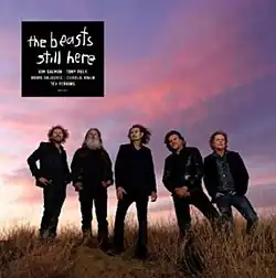A photo of five men standing in a row in a grassy field, in front of a cloudy sky at sunset.