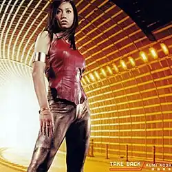 A body shot of a Japanese woman (Koda Kumi) standing in the middle of an underground tunnel, orange-tinted while the artist and song title are placed at the bottom corner.