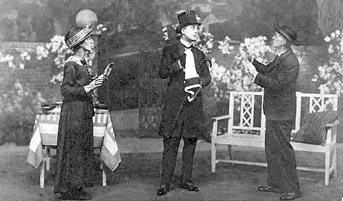 stage scene with man in full mourning costume centre, woman to his right and man in clerical garb to his left
