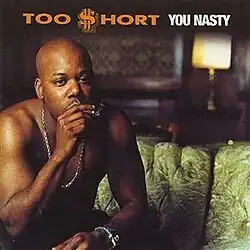 A photo of a shirtless Too Short in a hotel room, sitting down a green couch, smoking a cigar. Both the artist's name and album title appear above him, colored in orange and white respectively.