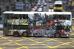 A bus with Optimus Prime and Chinese characters printed on its side drives across a street.