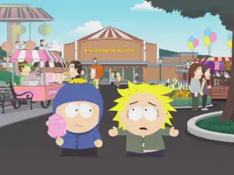 Two children, one in a blue jacket and the other in a green buttoned-shirt, stand in the middle of an amusement park.