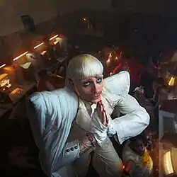 Joost Klein in a white costume looking upward and standing with hands held together