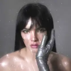 A close-up photograph of Benee with dark bangs, looking at the camera, wearing a metallic silver glove on her right hand which is resting against her face, set against a simple grey background with a superimposed sparkle effect