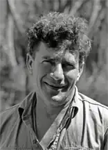 Black and white image of ornithologist Vincent Serventy, in about 1975 when he was around 59 years of age. It is a head and shoulders shot of white man with curly brown hair, wearing a work shirt, smiling into the lens.