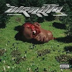 Bloody and gory image of a man's head being shot and beheaded, with his brain being fully exposed, the head is surrounded by nearby greenery. On the ground, there are small figures of people standing in front of the head celebrating the death.