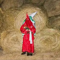 Cover art for In a Perfect World: a picture of two klansmen, one in red and one in white, in front of a stack of hay bales.