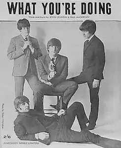 Black & white photo of the Beatles, with Lennon seated flanked by McCartney & Harrison and Starr reclining in front