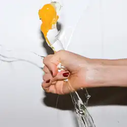 On a white wall, the hand of an unknown woman crushes an egg.