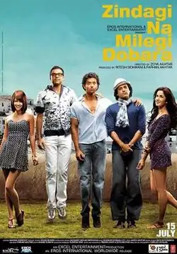 Five young Indian people stand on grass under a blue sky. From left, a young woman wearing a short black-and-white dress stands with her right leg slightly twisted. A man wearing glasses is jumping with his hands on back of the next person. A second man stares ahead, putting his hands on the shoulders of the third man. The third man wears a hat and a scarf, with his hands crossed in front. On the right is a woman wearing a short dress; her right leg is twisted backwards and she holds her elbow stretched out and her left arm to her right.